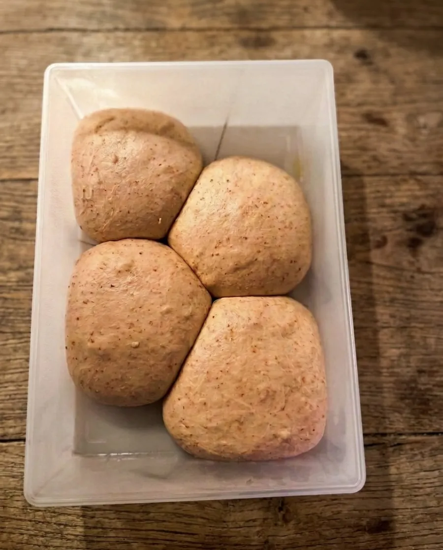 Four balls of bread dough resting in a container on a wooden worktop